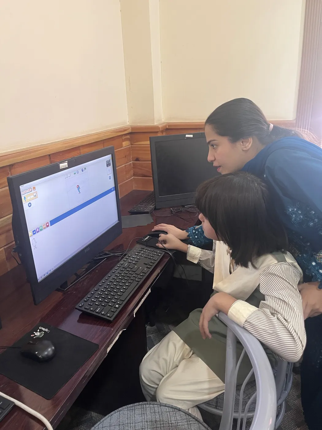 A teacher helping a student at a computer in the school lab