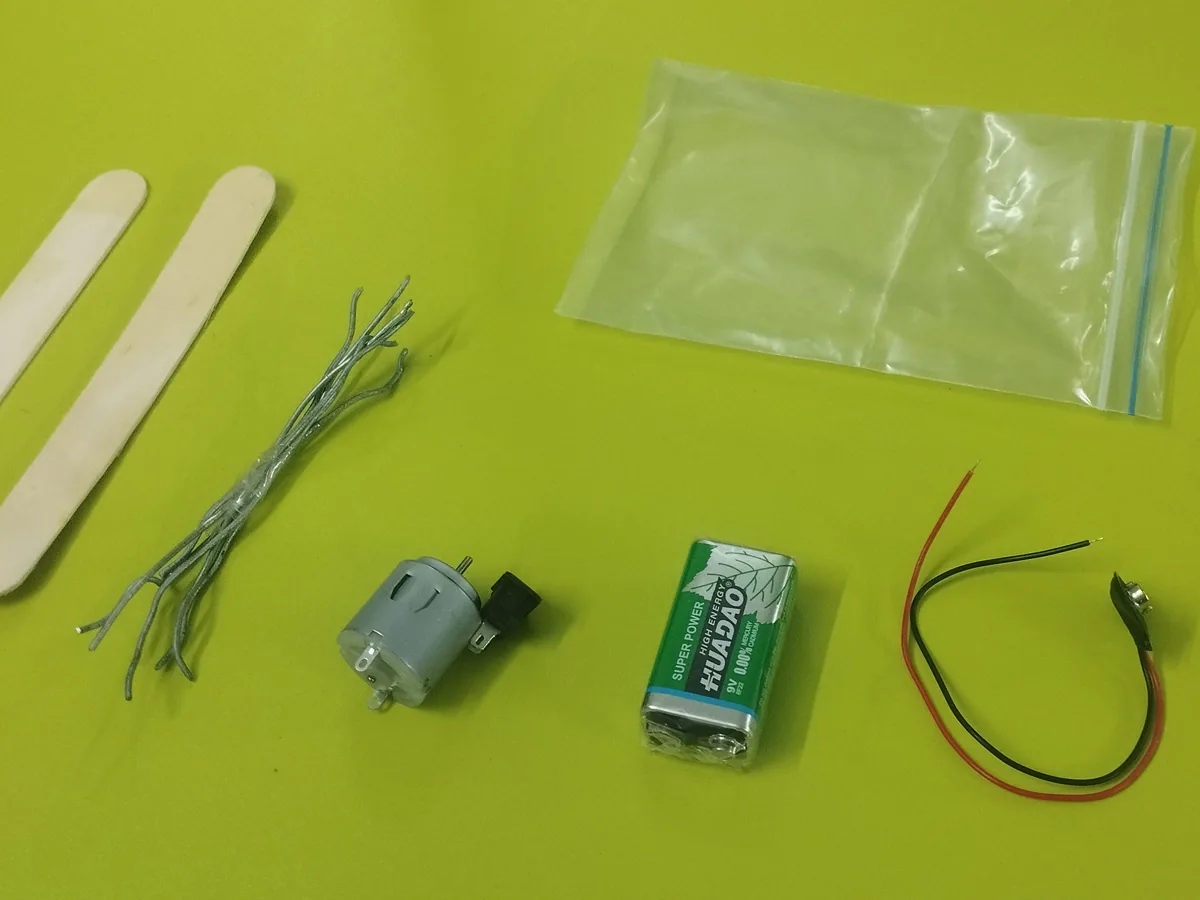 Spider Bot parts laid out: motor, battery, wires and craft sticks